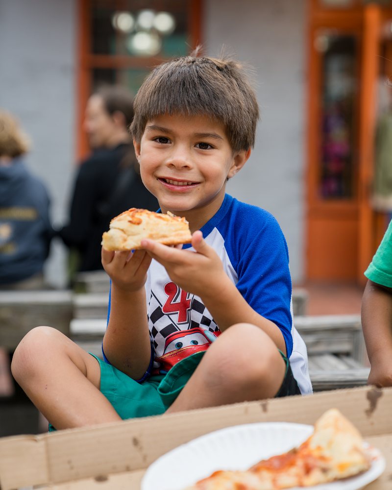 Boy smiling while holding a slice of pizza at Vinnie Van Go Gos in Savannah City Market